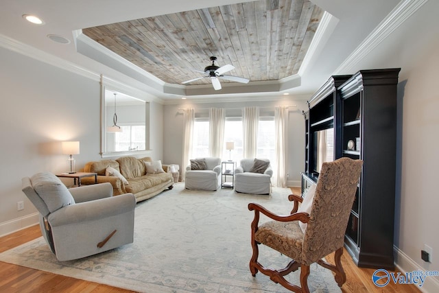 living area with baseboards, a raised ceiling, light wood-style flooring, and ornamental molding