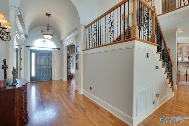 entrance foyer featuring hardwood / wood-style floors, baseboards, visible vents, high vaulted ceiling, and stairs