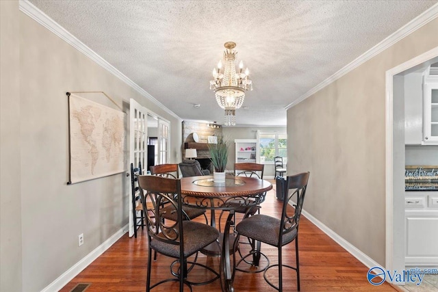 dining room featuring a notable chandelier, ornamental molding, a textured ceiling, and dark wood-type flooring