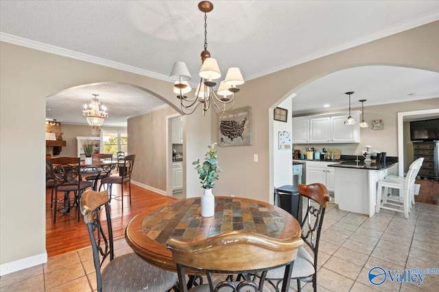 dining space with an inviting chandelier, light hardwood / wood-style flooring, ornamental molding, and a textured ceiling