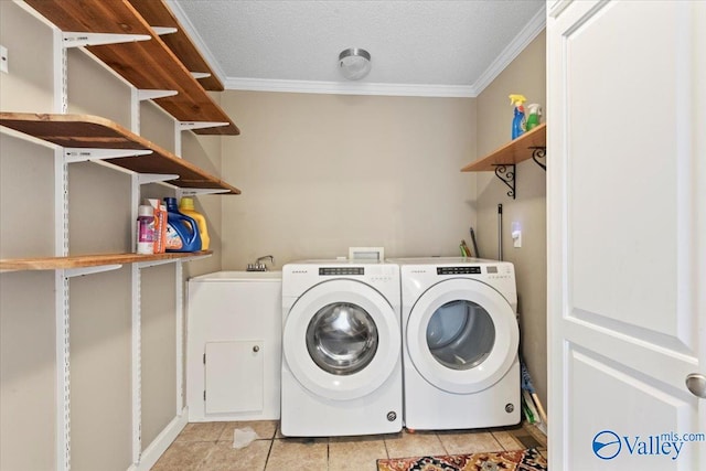 clothes washing area featuring ornamental molding, a textured ceiling, light tile patterned floors, and washing machine and dryer