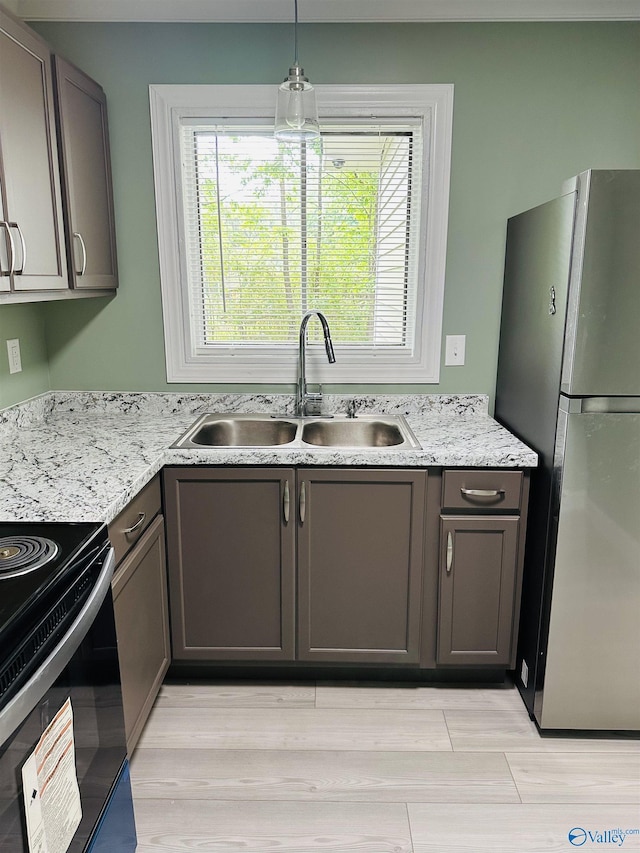 kitchen featuring electric range oven, pendant lighting, refrigerator, sink, and light stone counters