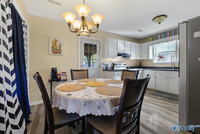 dining area with sink, light hardwood / wood-style floors, a textured ceiling, and an inviting chandelier