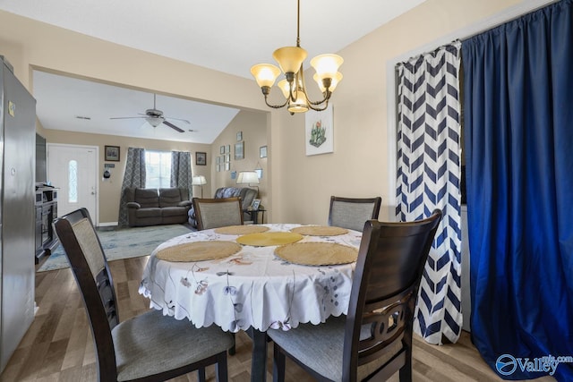 dining space featuring hardwood / wood-style floors, ceiling fan with notable chandelier, and vaulted ceiling