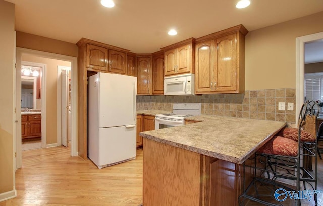 kitchen with kitchen peninsula, white appliances, tasteful backsplash, light hardwood / wood-style flooring, and a breakfast bar area