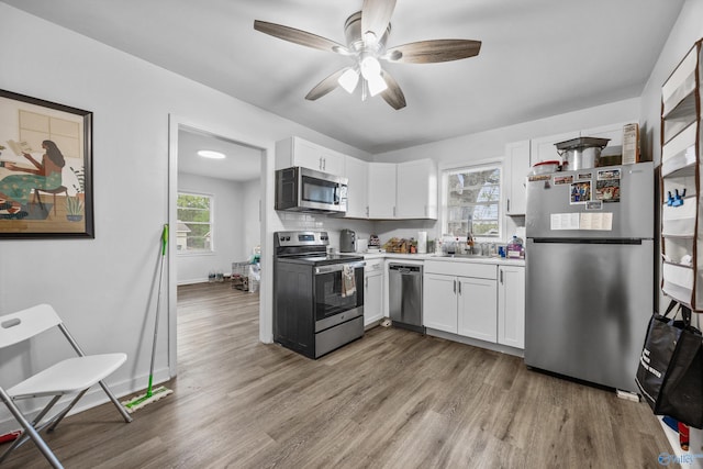 kitchen with appliances with stainless steel finishes, wood finished floors, white cabinetry, and a sink