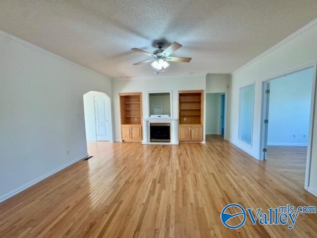 unfurnished living room with crown molding, a textured ceiling, light wood-type flooring, built in features, and ceiling fan