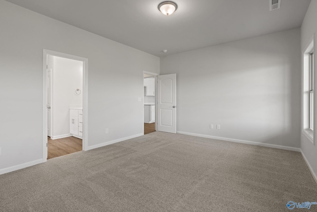 unfurnished bedroom featuring connected bathroom and light carpet