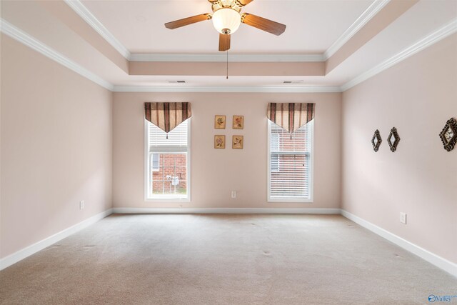 carpeted empty room featuring a raised ceiling, healthy amount of natural light, ornamental molding, and ceiling fan