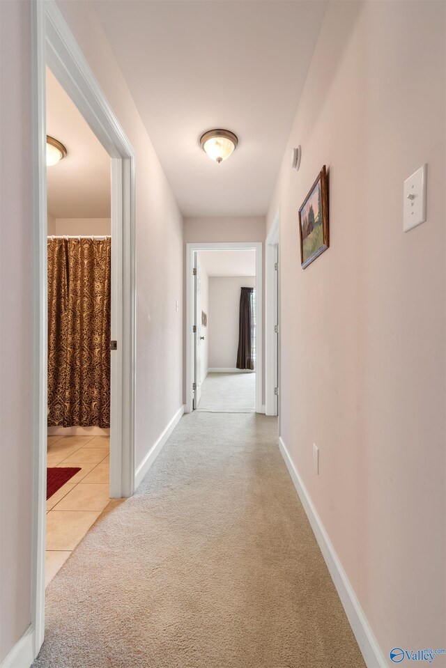 hallway featuring carpet floors, baseboards, and tile patterned floors
