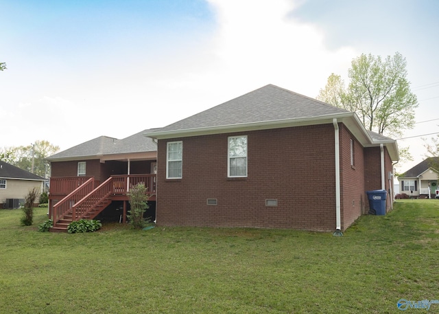 back of property with roof with shingles, central air condition unit, stairway, brick siding, and a lawn