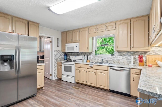 kitchen featuring tasteful backsplash, appliances with stainless steel finishes, light countertops, a sink, and light wood-type flooring
