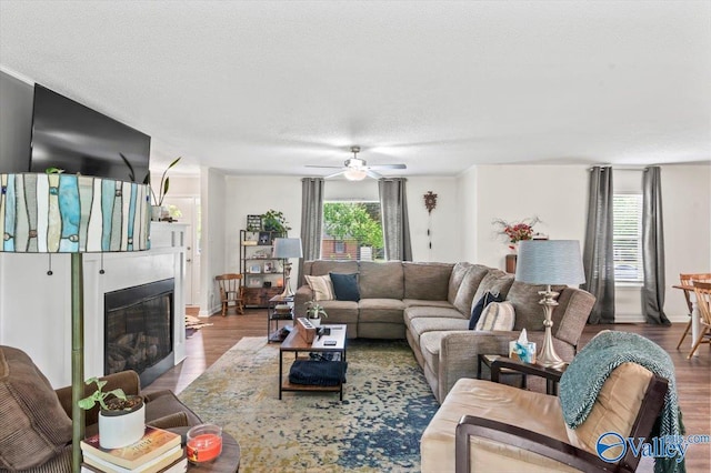 living area with a ceiling fan, a textured ceiling, wood finished floors, and a glass covered fireplace