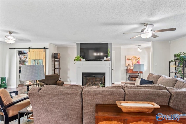 living room featuring a barn door, a ceiling fan, a textured ceiling, and a glass covered fireplace