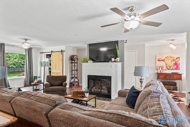 living area with a barn door, wood finished floors, a ceiling fan, and a textured ceiling