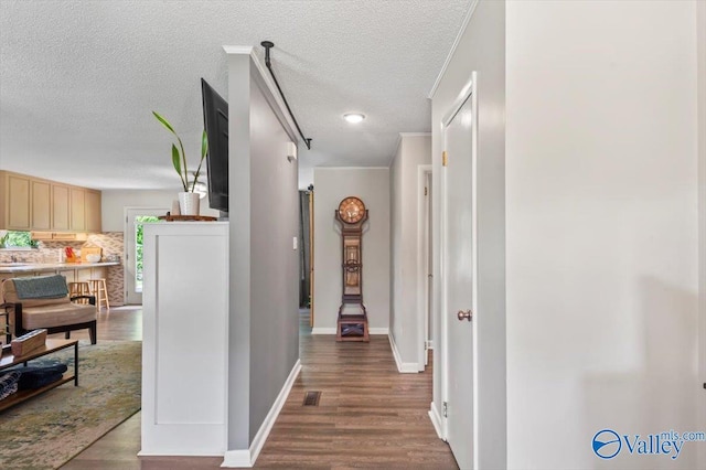 hallway with a textured ceiling, wood finished floors, visible vents, and baseboards