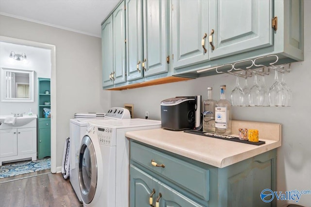 washroom with wood finished floors, independent washer and dryer, cabinet space, a sink, and crown molding