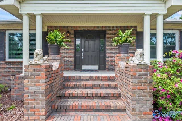 view of exterior entry featuring a porch and brick siding