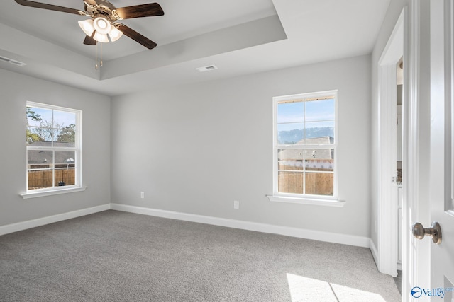 unfurnished bedroom featuring a tray ceiling, carpet, visible vents, and baseboards