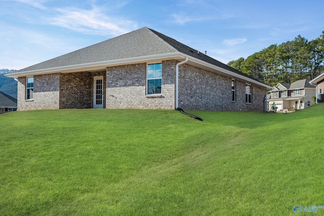 rear view of property with a shingled roof, brick siding, and a yard