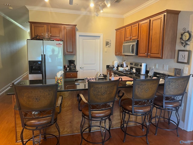 kitchen featuring stainless steel appliances, a breakfast bar, dark wood-type flooring, kitchen peninsula, and ornamental molding