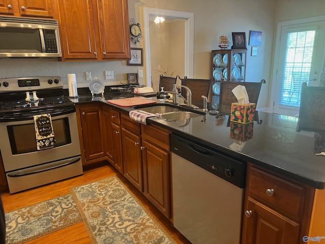 kitchen featuring light wood-type flooring, dark stone countertops, sink, and stainless steel appliances