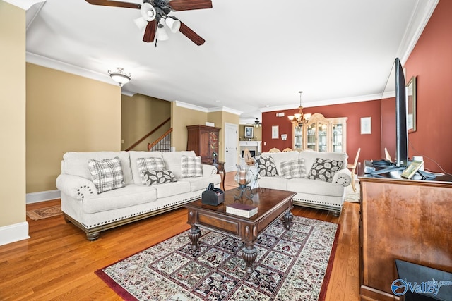 living room with ceiling fan with notable chandelier, baseboards, wood finished floors, ornamental molding, and stairway