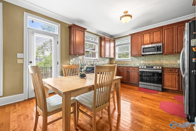 kitchen featuring a healthy amount of sunlight, decorative backsplash, appliances with stainless steel finishes, light wood-style floors, and ornamental molding