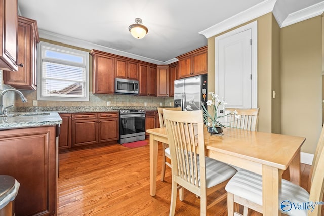 kitchen with appliances with stainless steel finishes, a sink, light wood-style flooring, and tasteful backsplash