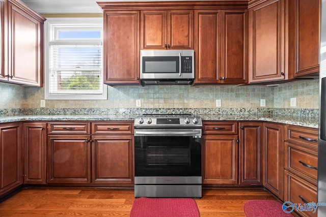 kitchen featuring light wood-style flooring, appliances with stainless steel finishes, light stone countertops, and tasteful backsplash