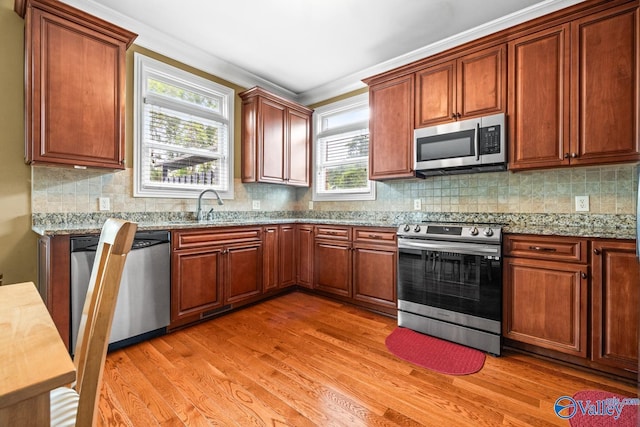 kitchen with crown molding, appliances with stainless steel finishes, light wood-type flooring, a sink, and light stone counters