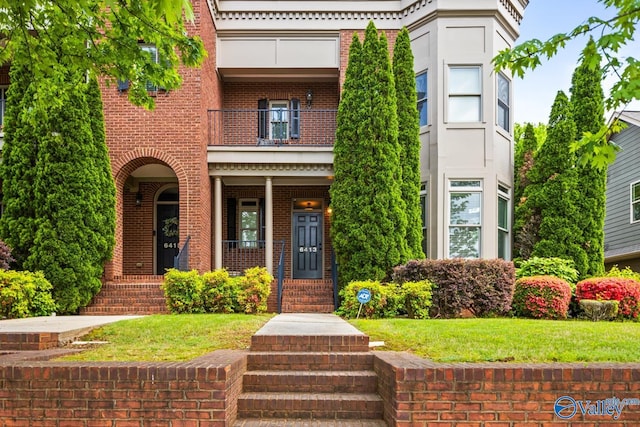 view of front facade with a balcony, a front yard, a porch, and brick siding