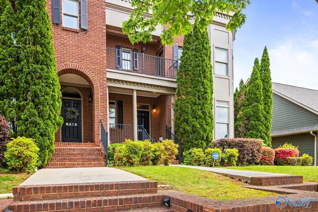 doorway to property featuring a porch, brick siding, a balcony, and a lawn