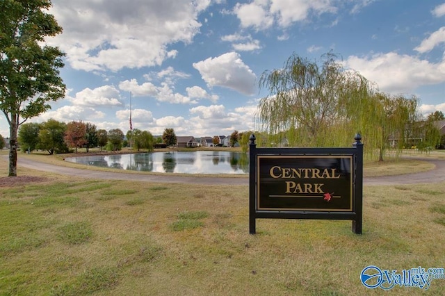 community / neighborhood sign featuring a lawn and a water view