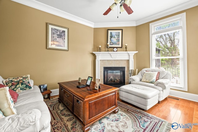 living room with a ceiling fan, visible vents, a fireplace, baseboards, and ornamental molding