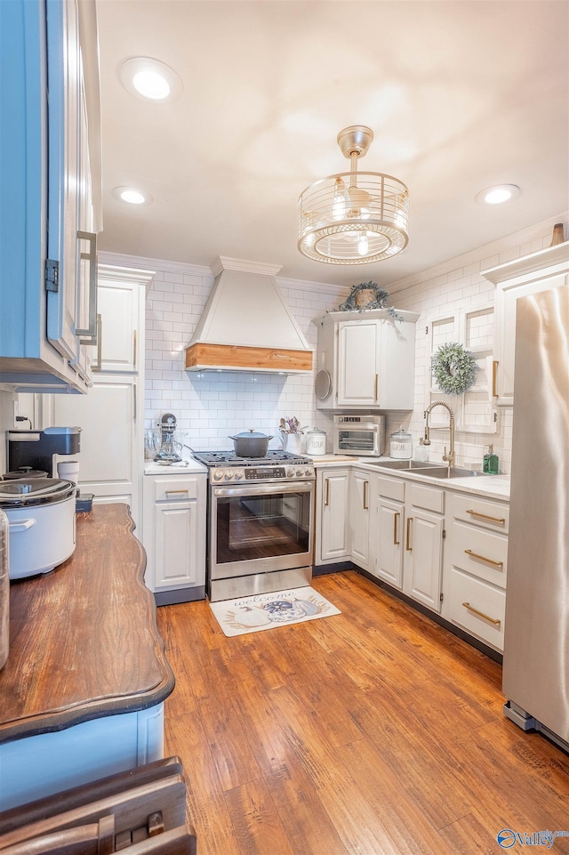 kitchen featuring premium range hood, pendant lighting, sink, white cabinets, and stainless steel appliances