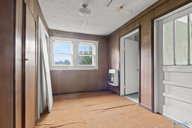 hallway featuring heating unit, light colored carpet, and wooden walls