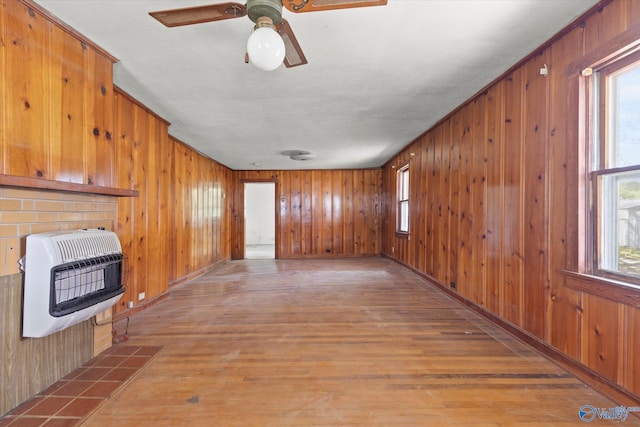 unfurnished living room with wood-type flooring, heating unit, wood walls, and ceiling fan