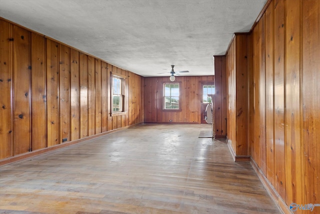 unfurnished room with wood walls, light wood-type flooring, and ceiling fan