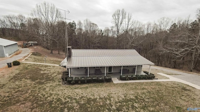 view of front of house with a porch, a front yard, metal roof, and a wooded view