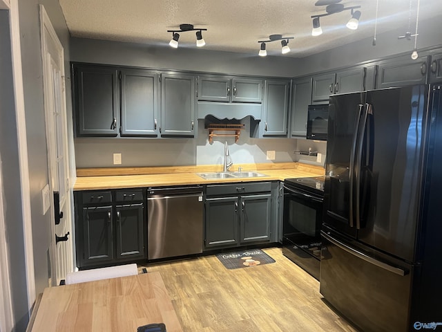 kitchen with wood counters, sink, a textured ceiling, light hardwood / wood-style flooring, and black appliances