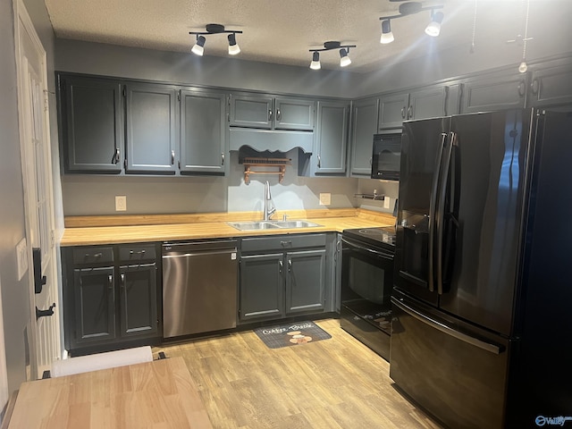 kitchen featuring butcher block countertops, sink, a textured ceiling, light hardwood / wood-style flooring, and black appliances