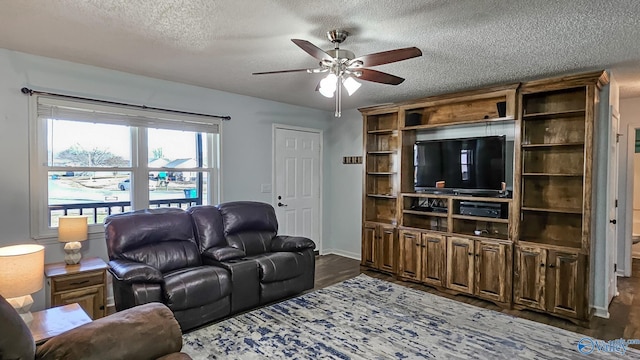 living room featuring dark wood-type flooring, ceiling fan, and a textured ceiling