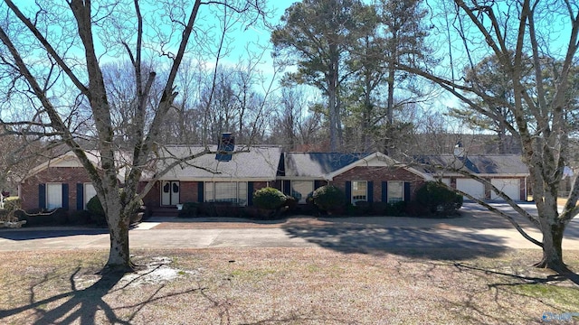 ranch-style home featuring a garage, driveway, a chimney, and brick siding