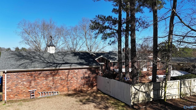 view of home's exterior featuring brick siding, fence, a chimney, and roof with shingles