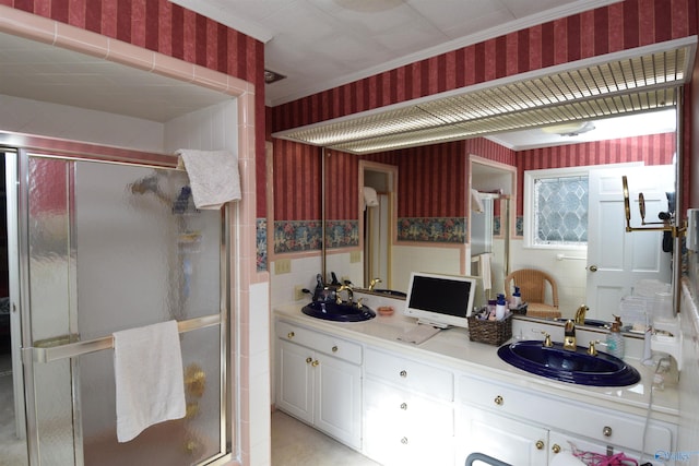 bathroom featuring double vanity, wallpapered walls, a sink, and a stall shower