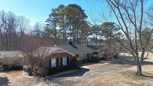 view of front of house with roof with shingles, a chimney, concrete driveway, and brick siding