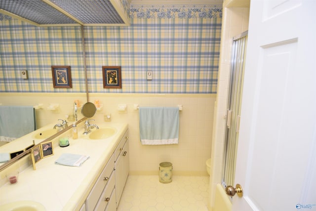 full bath with wallpapered walls, a shower with door, a sink, and a wainscoted wall