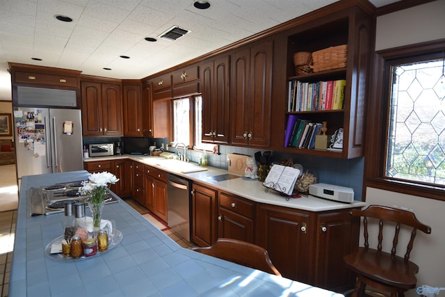 kitchen with tile counters, stainless steel appliances, a healthy amount of sunlight, open shelves, and a sink