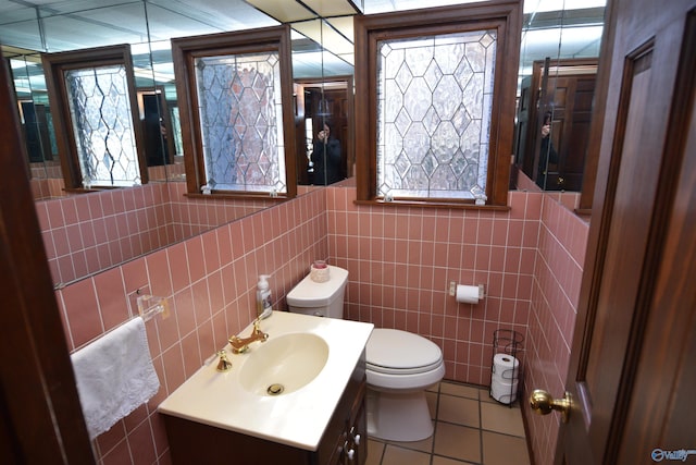 half bathroom with toilet, tile walls, vanity, and tile patterned floors